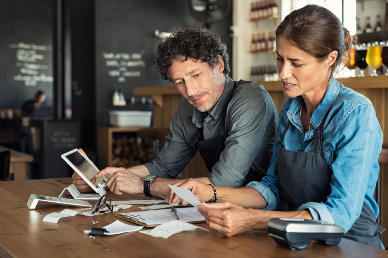 Two restaurant owners review their restaurant technology invoices and expenses.